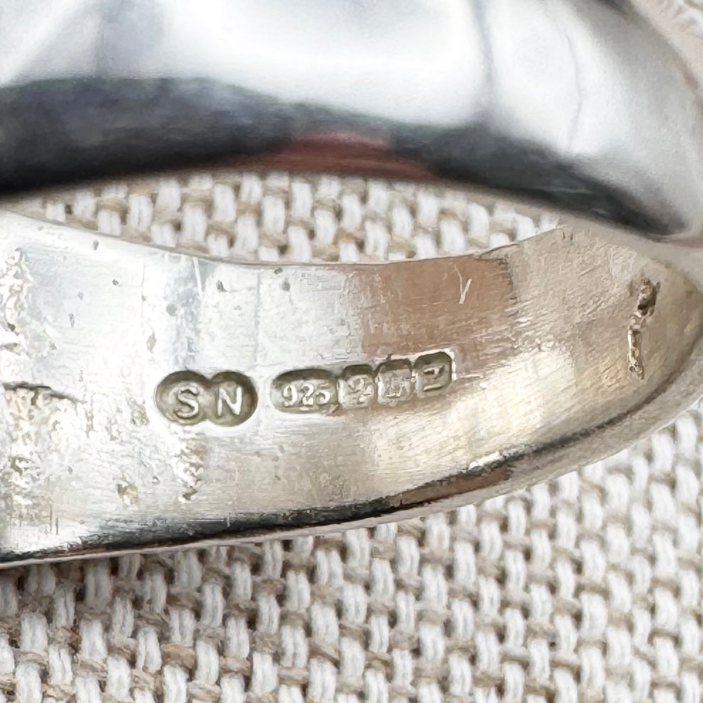 Close-up of a silver ring with visible hallmarks on a textured fabric background