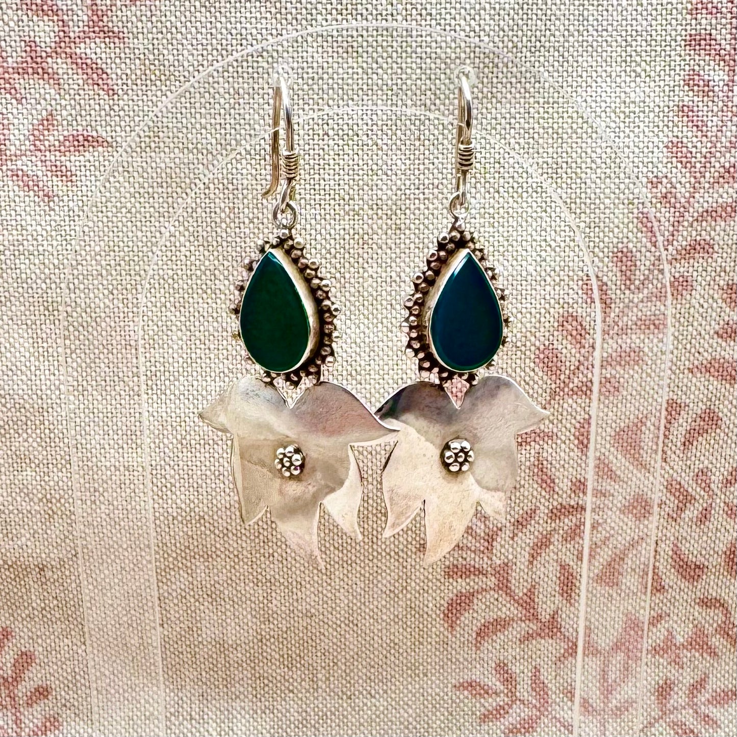 Pair of earrings with green teardrop stones and floral designs on a textured fabric background