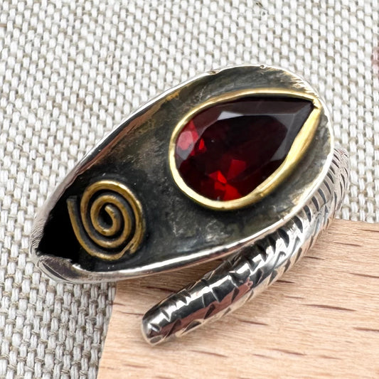 Silver ring with a red gemstone and gold accents on a textured fabric background