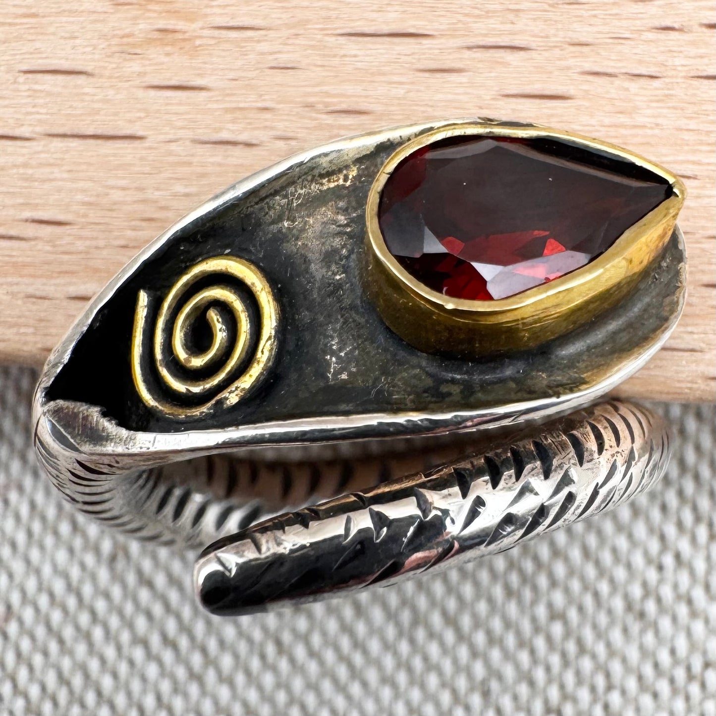 Silver ring with a red stone and gold spiral design on a wooden surface