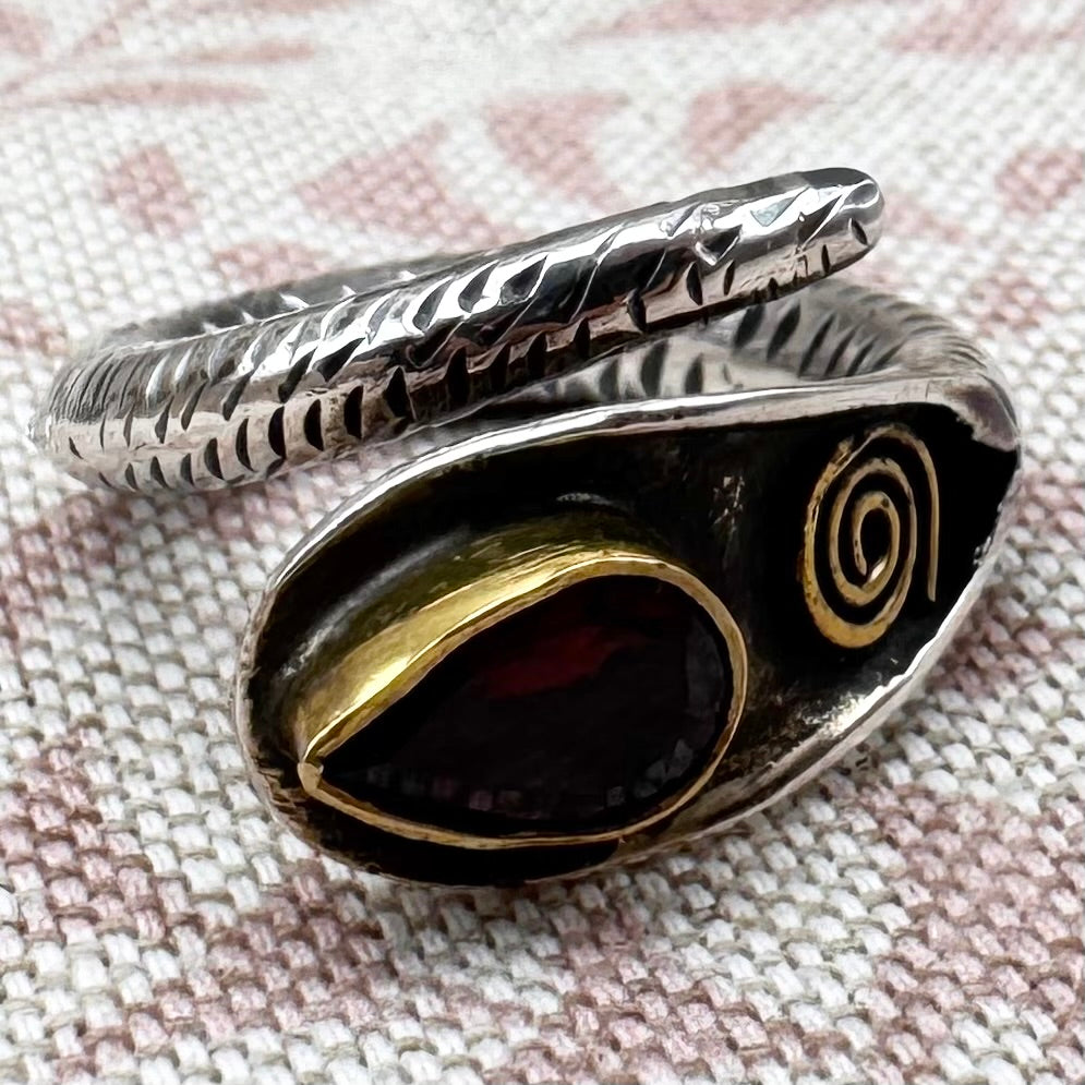 Silver ring with a red stone and gold accents on a textured fabric background