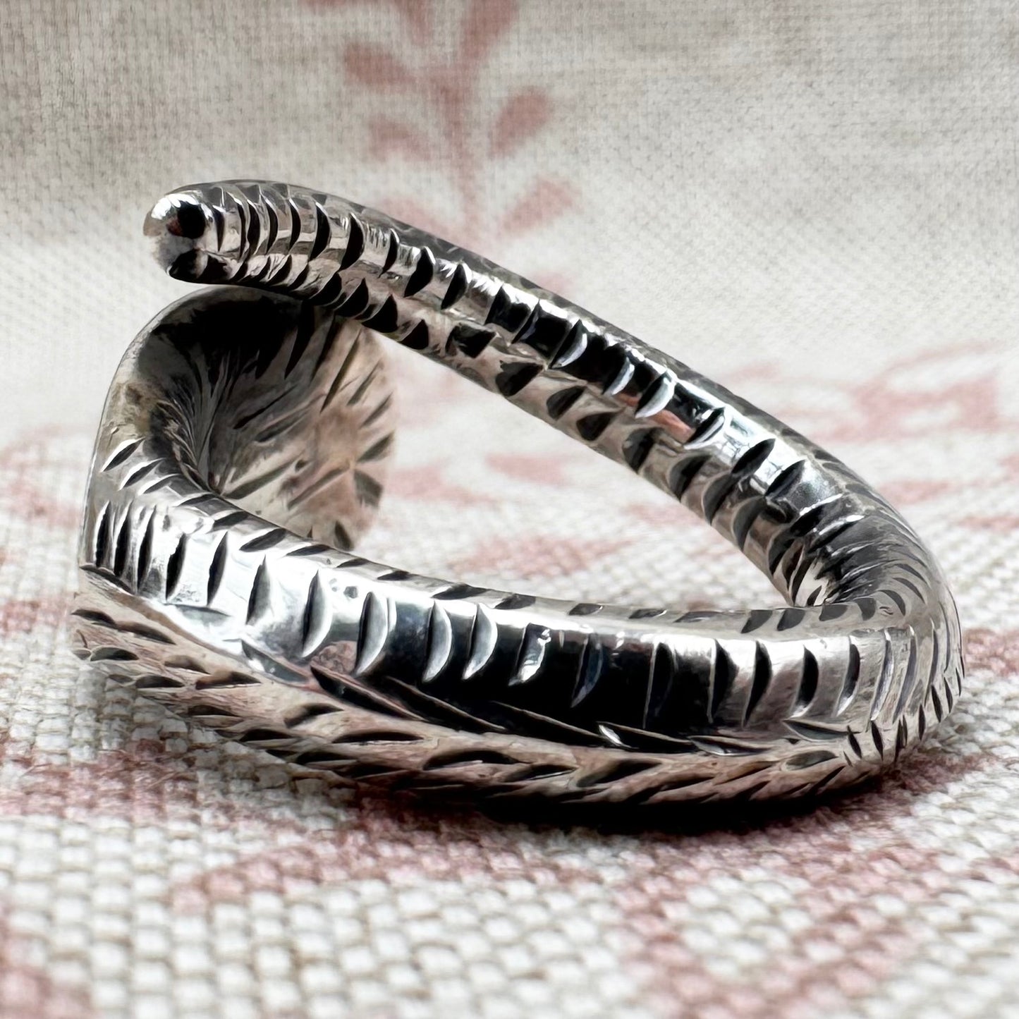 Silver snake-shaped ring on a textured fabric background