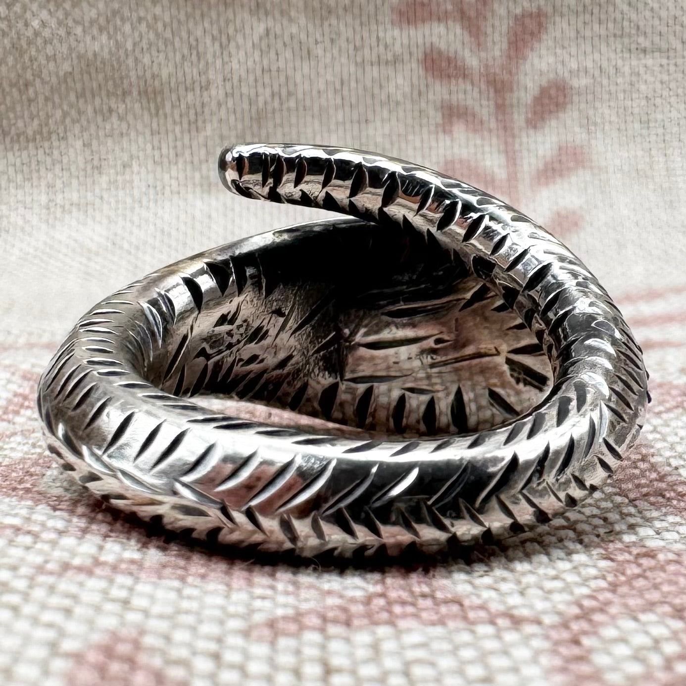 Silver snake-shaped ring on a textured fabric background