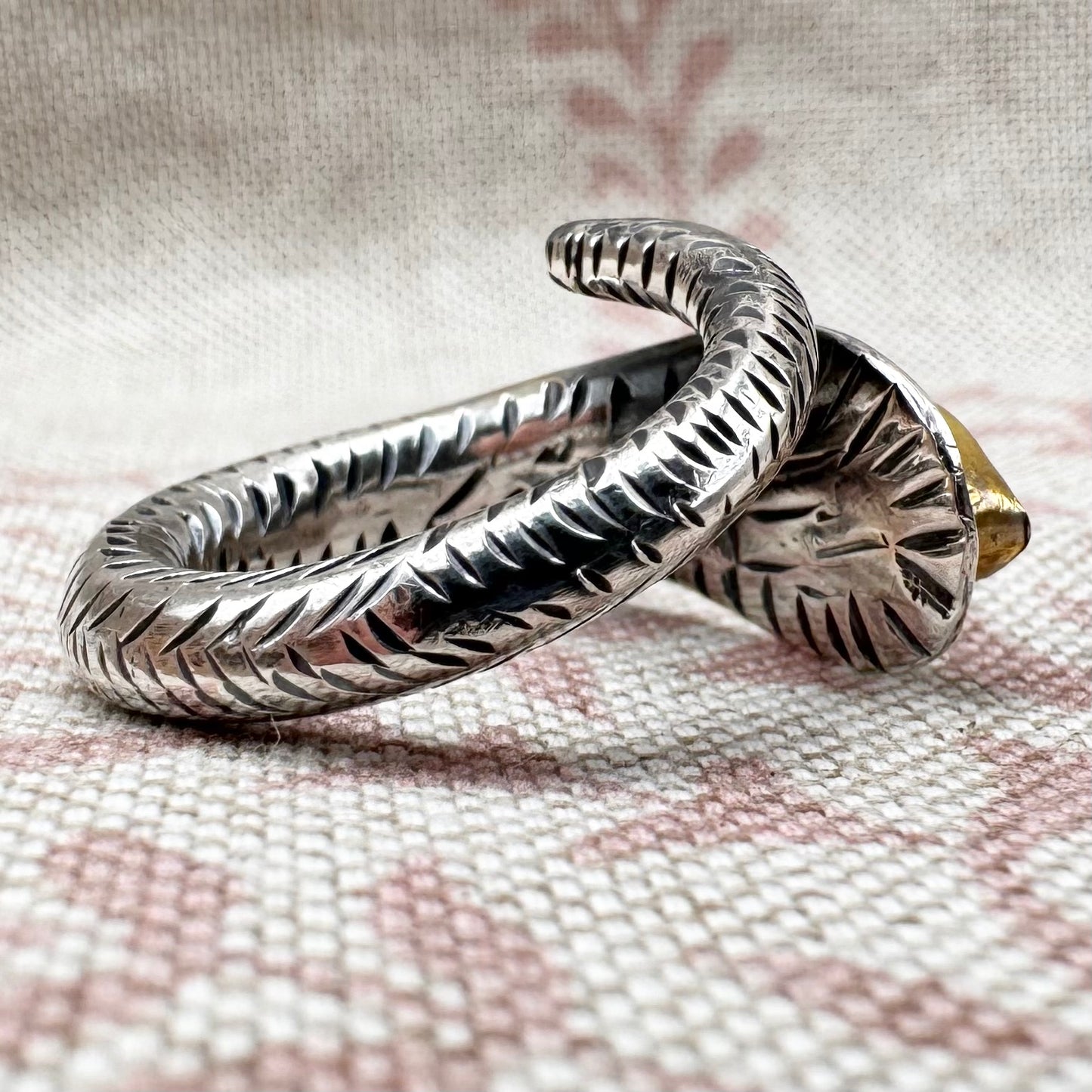 Silver ring with intricate design on a textured fabric background