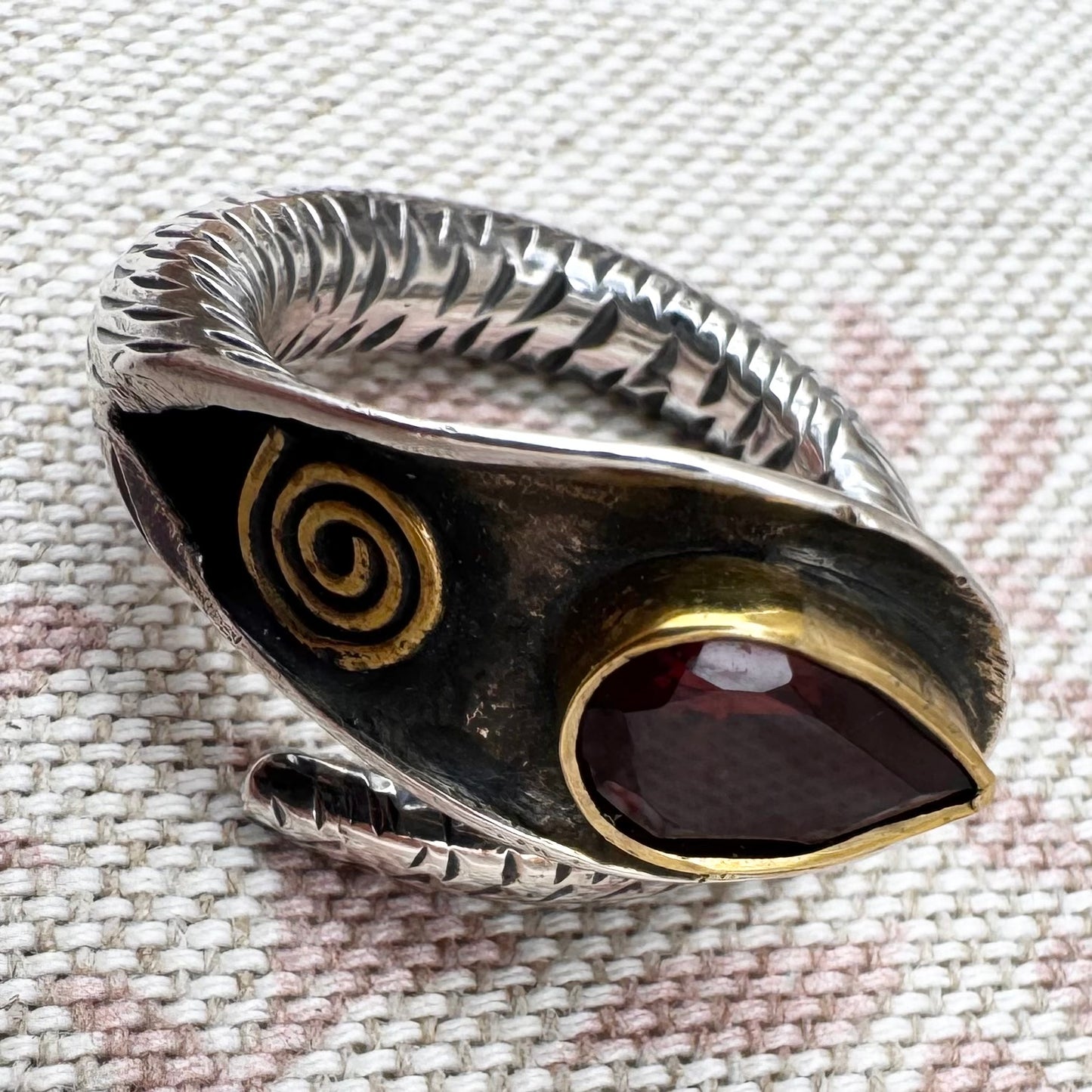 Silver ring with a red stone and gold accents on a textured fabric background