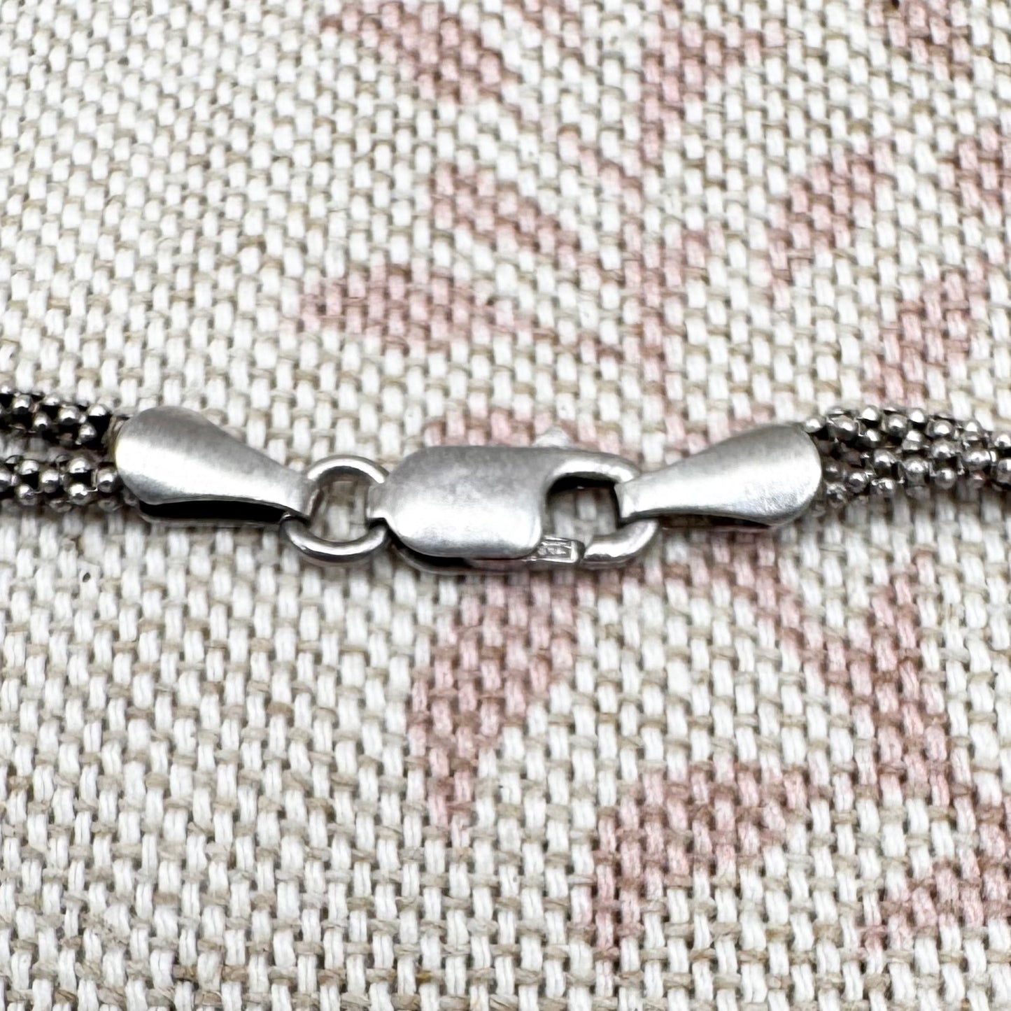 Close-up of a silver bracelet clasp on a textured fabric background