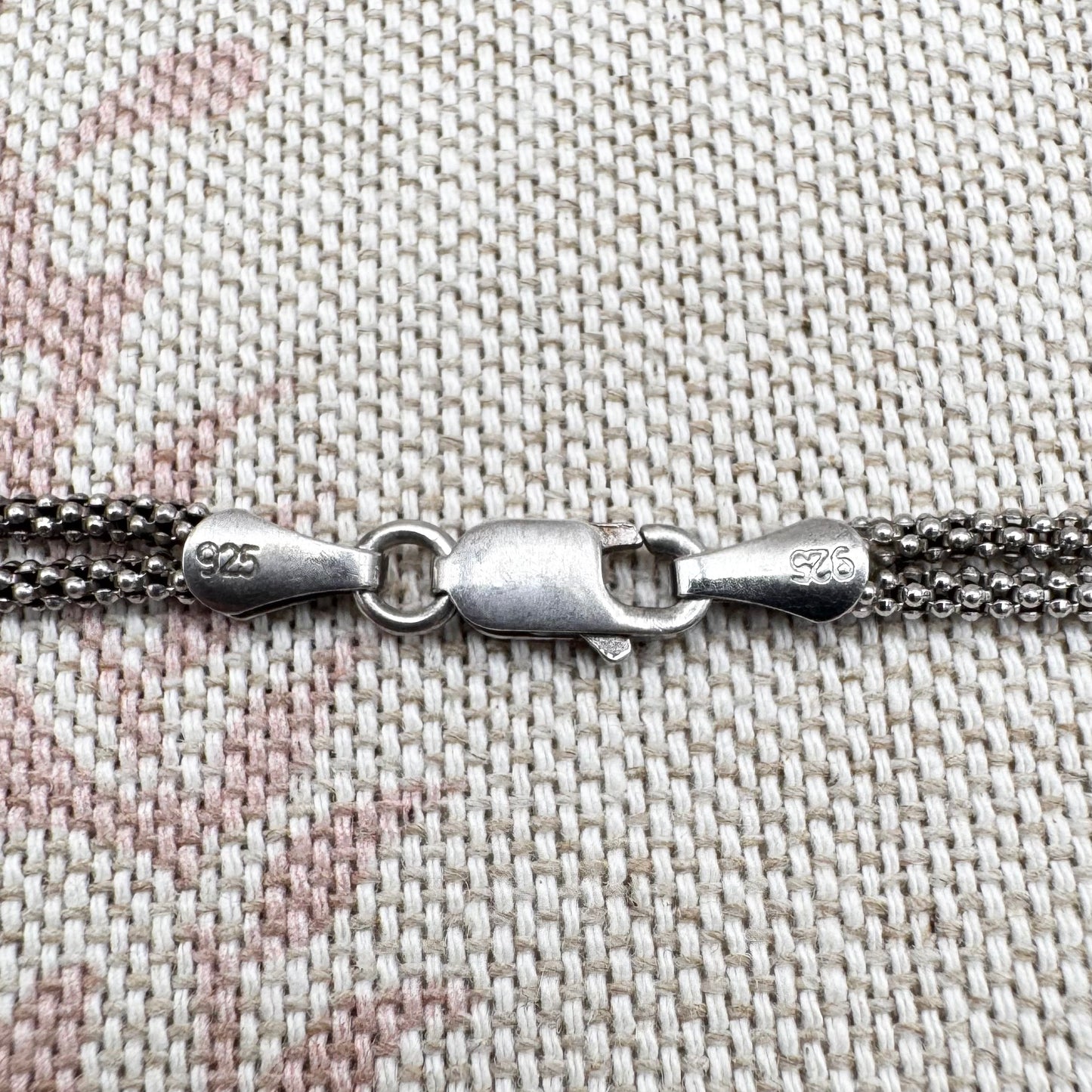 Close-up of a silver chain with clasp on a textured fabric background
