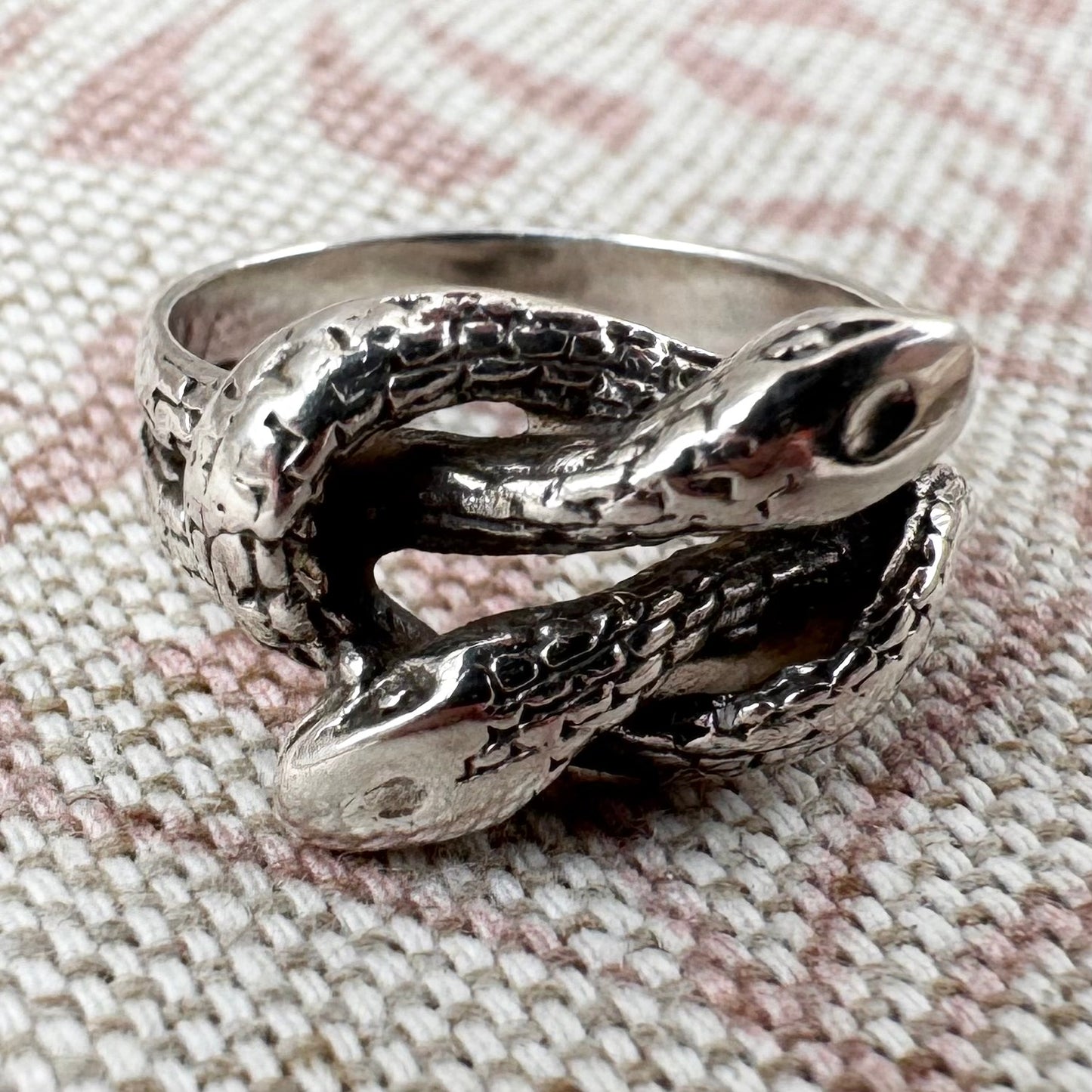 Silver snake-shaped ring on a textured fabric background