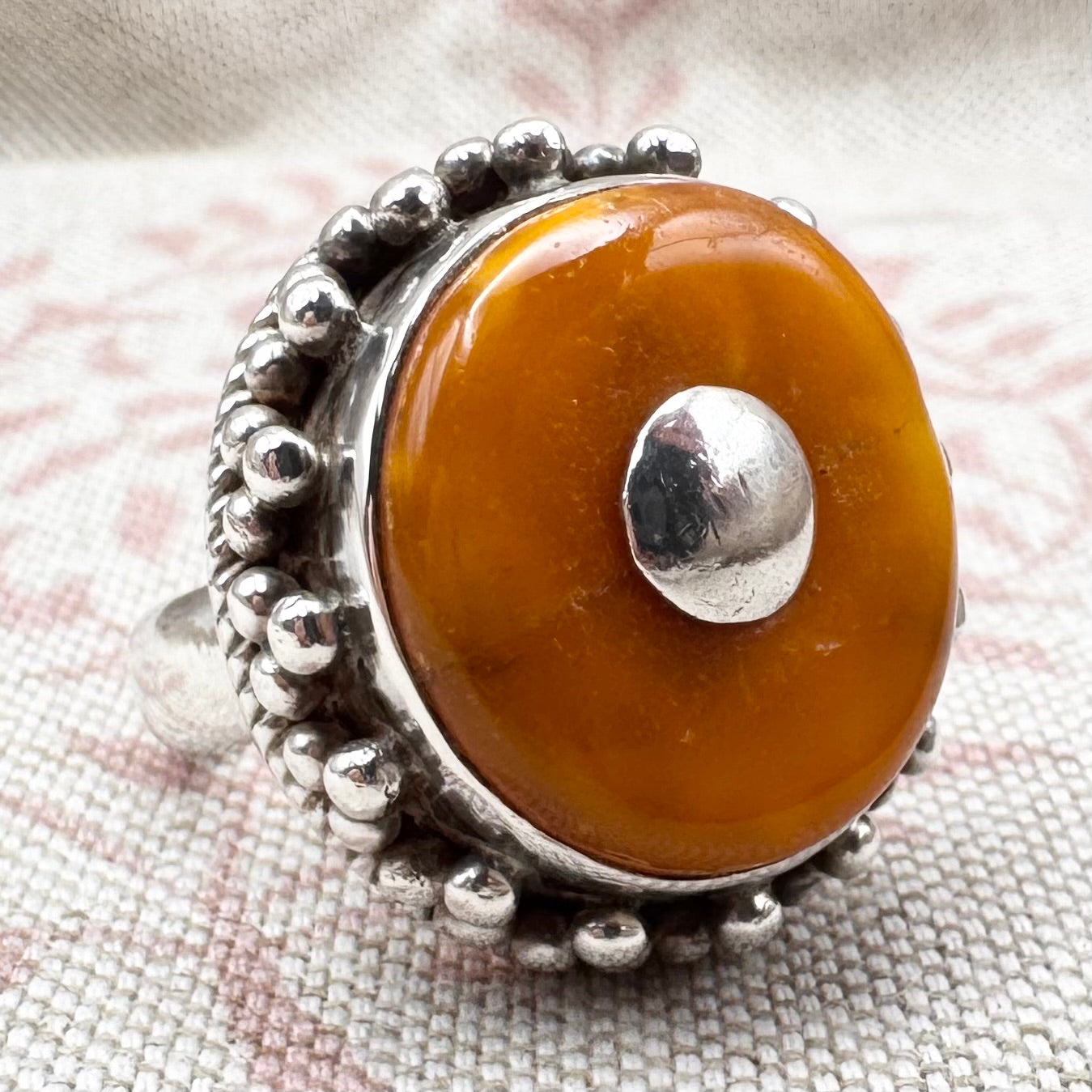 Silver ring with a large amber stone on a textured fabric background