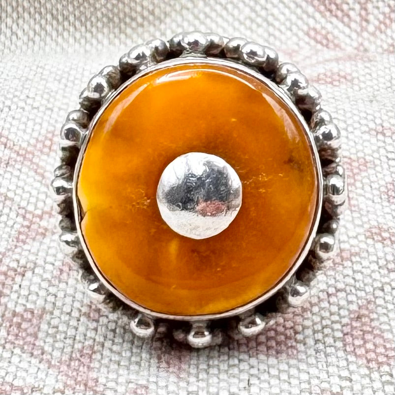 Ring with amber stone and silver band on a textured fabric background
