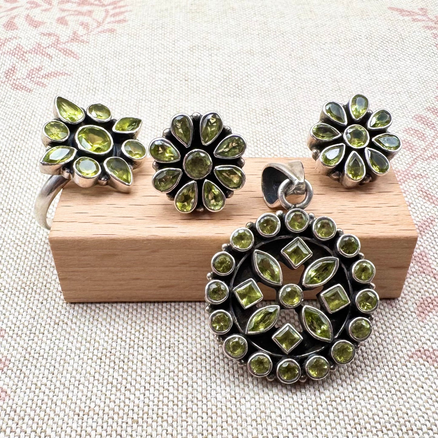 Green peridot jewellery set on a wooden block and light coloured fabric background