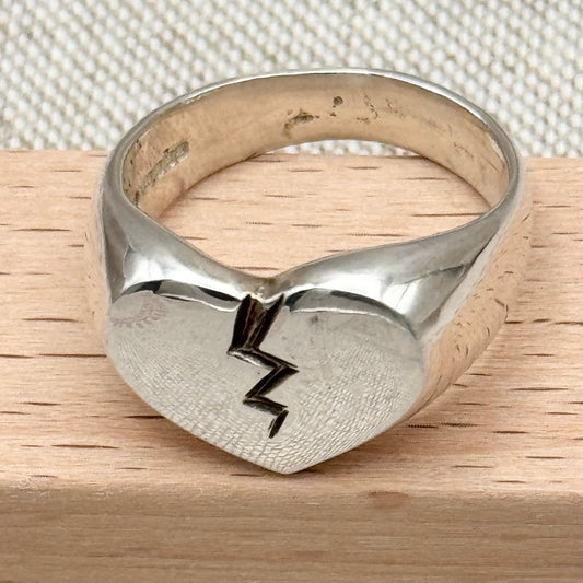 Silver ring with heart and lightning bolt design on a wooden surface