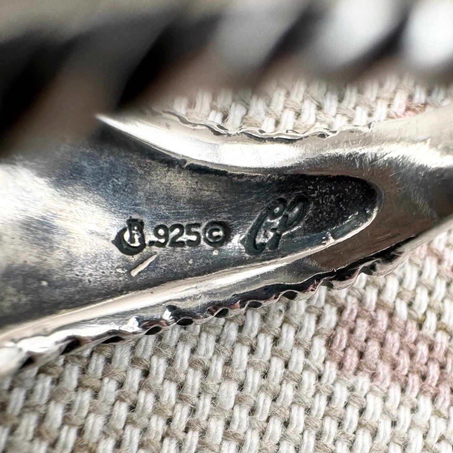 Close-up of a silver ring with '925' mark, alongside the silver marks for Carolyn Pollack and Relllios on a textured fabric background