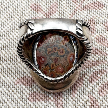 Silver ring with a textured stone on a fabric background