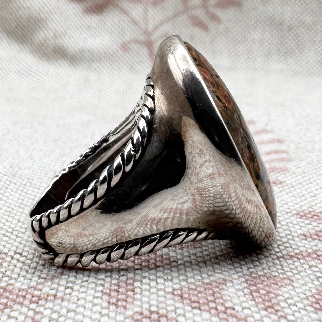 Silver ring with intricate design on a textured fabric background