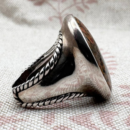 Silver ring with intricate design on a textured fabric background