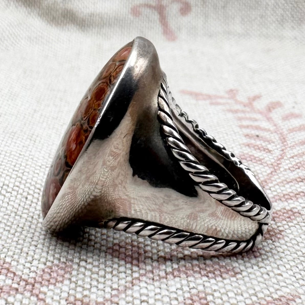 large  silver ring with intricate designs on a textured fabric background