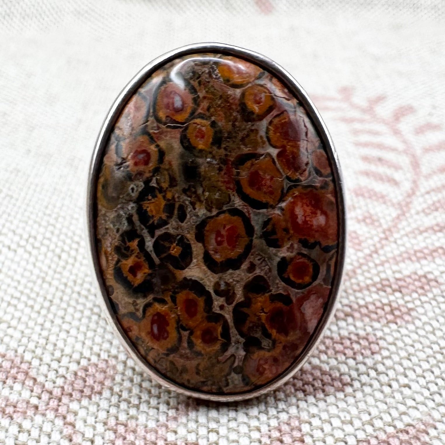 Oval-shaped stone with brown and black patterns on a textured fabric background