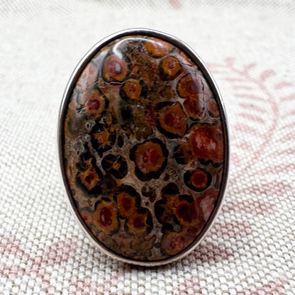 Oval-shaped stone with brown and black patterns on a textured fabric background