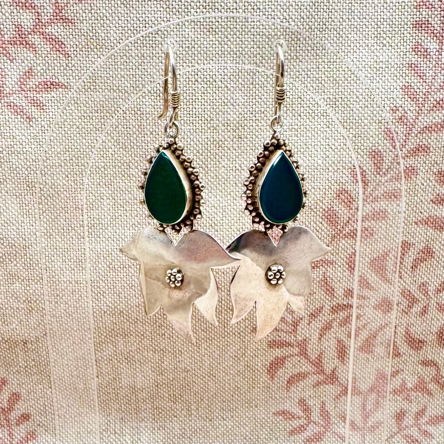 Pair of earrings with green teardrop stones and floral designs on a textured fabric background