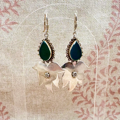 Pair of earrings with green teardrop stones and floral designs on a textured fabric background
