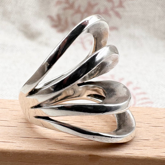 Silver ring with a wavy design on a wooden surface
