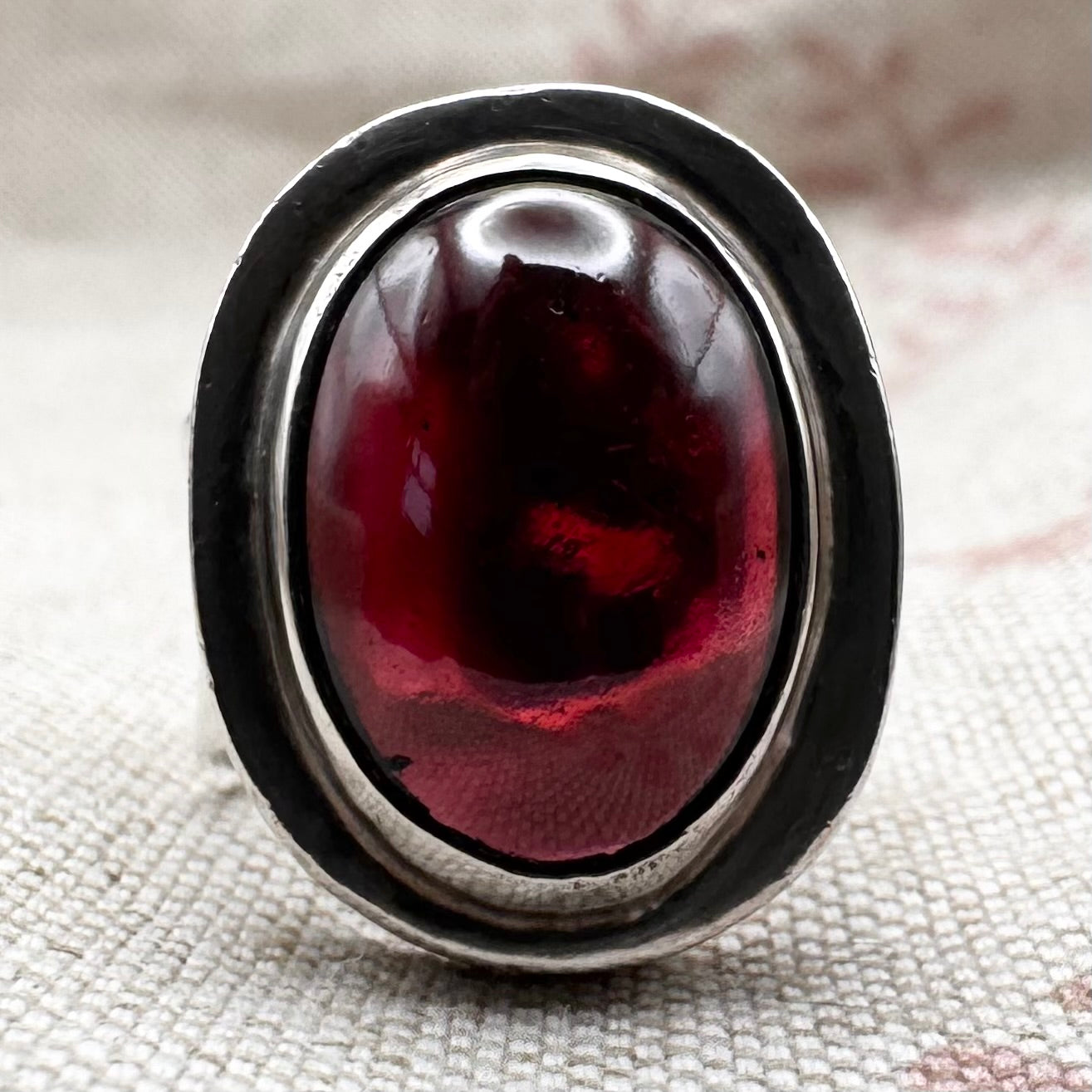 Ring with a red stone and silver band on a textured fabric background