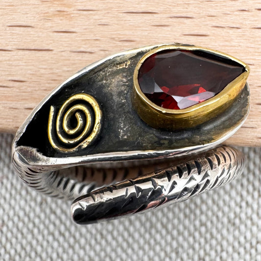 Silver ring with a red stone and gold spiral design on a wooden surface