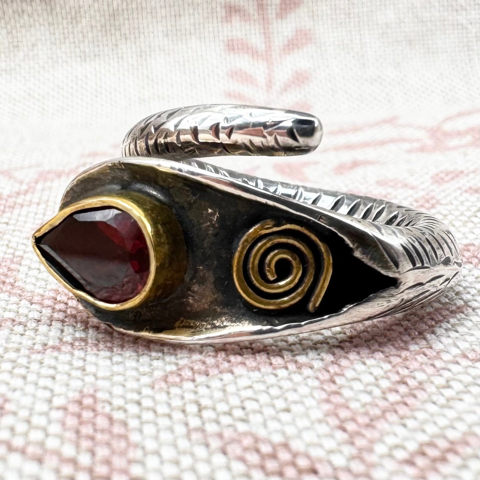 Silver ring with a red stone and spiral design on a textured fabric background