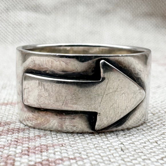 Silver ring with an arrow design on a textured fabric background