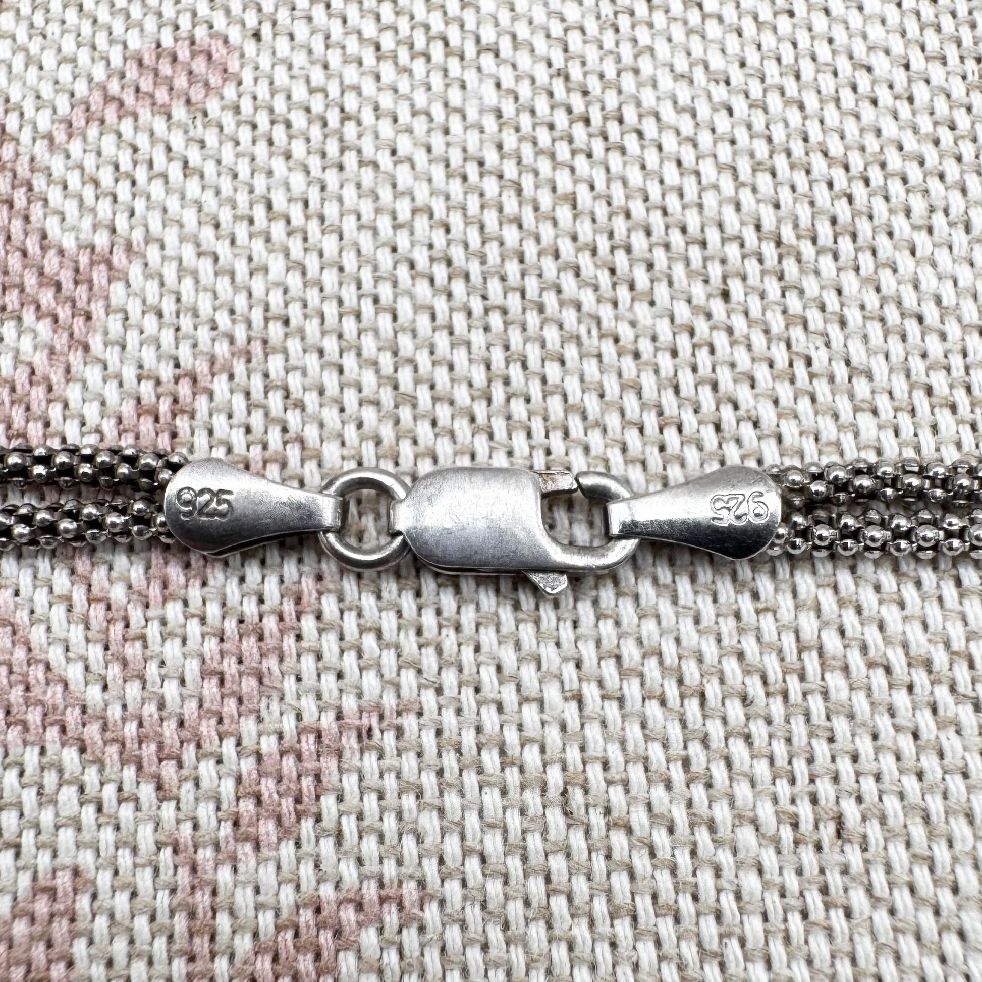 Close-up of a silver chain with clasp on a textured fabric background