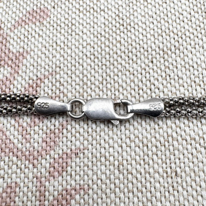 Close-up of a silver chain with clasp on a textured fabric background