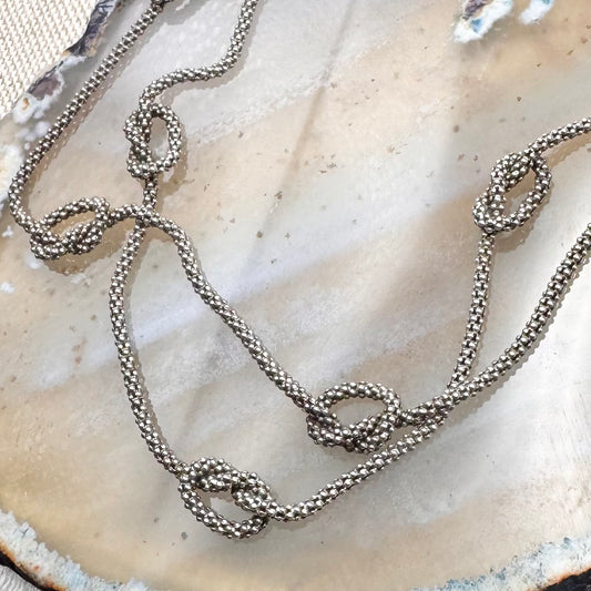 Silver chain necklace on a textured beige surface