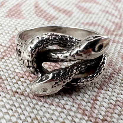 Silver snake-shaped ring on a textured fabric background