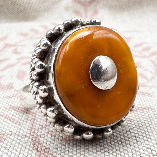 Silver ring with a large amber stone on a textured fabric background