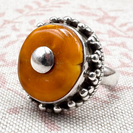 Silver ring with a large amber stone on a textured fabric background