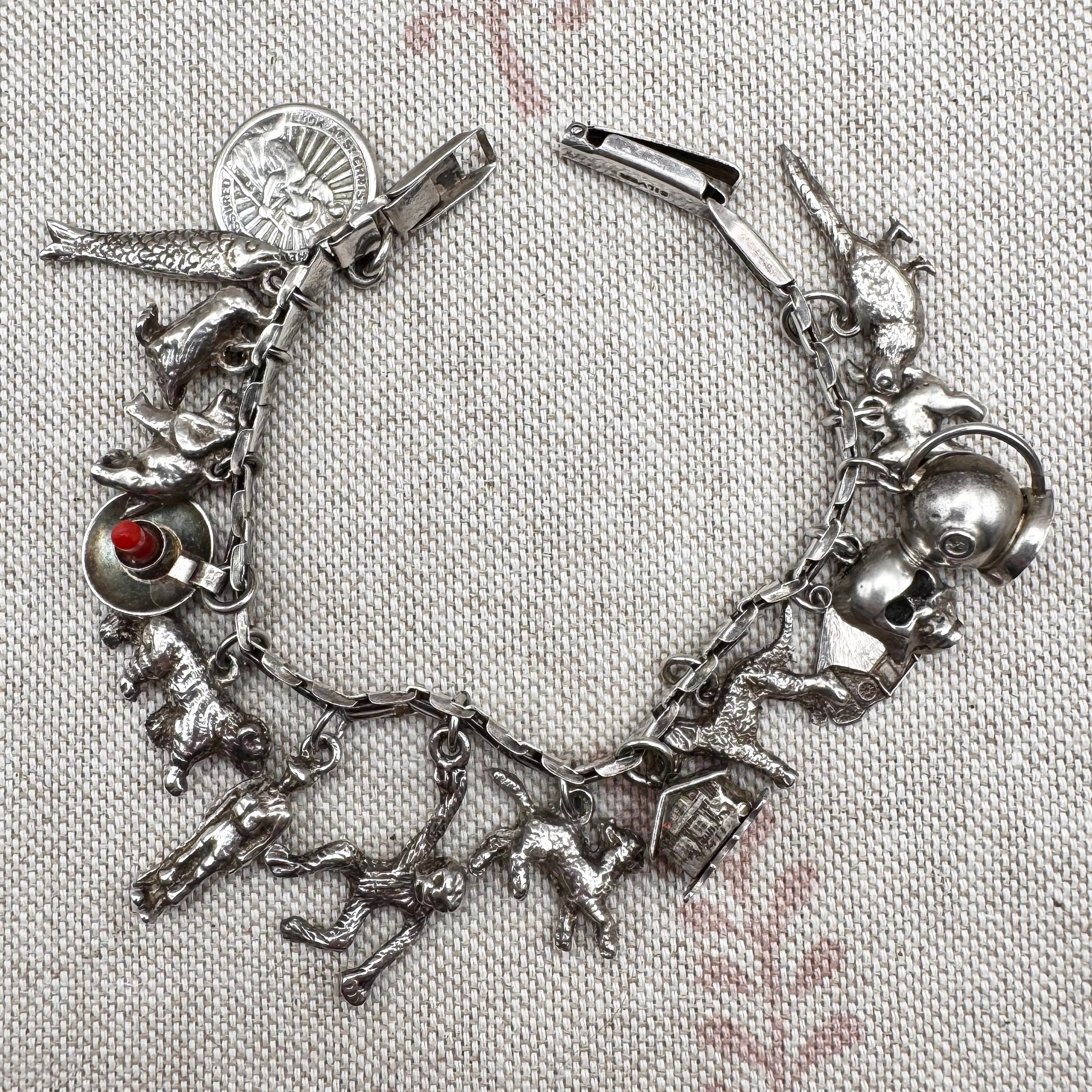 Silver charm bracelet with various charms on a textured fabric background