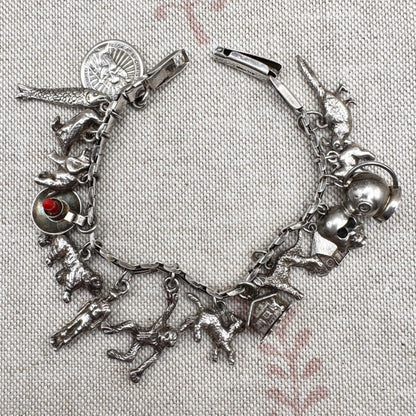 Silver charm bracelet with various charms on a textured fabric background