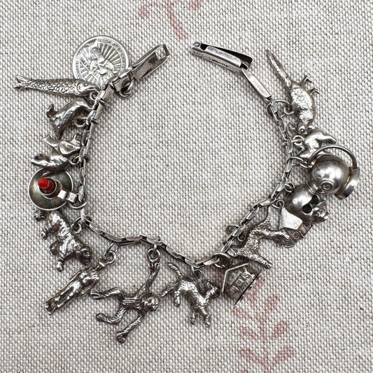 Silver charm bracelet with various charms on a textured fabric background