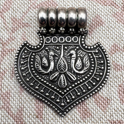 Silver pendant with intricate design on a textured fabric background