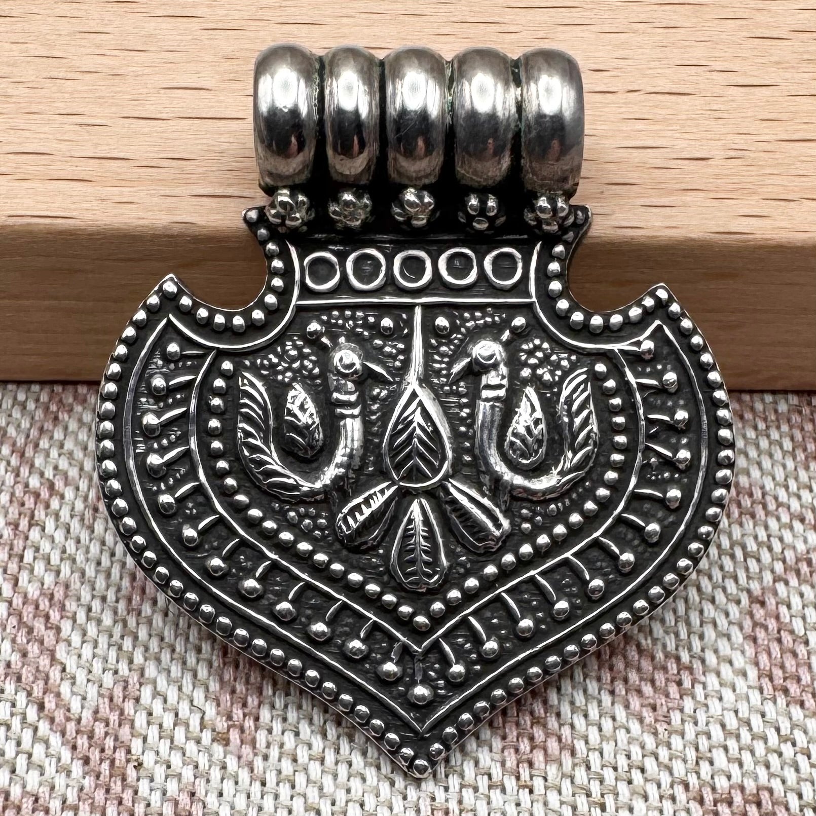 Silver pendant with intricate design on a textured fabric background
