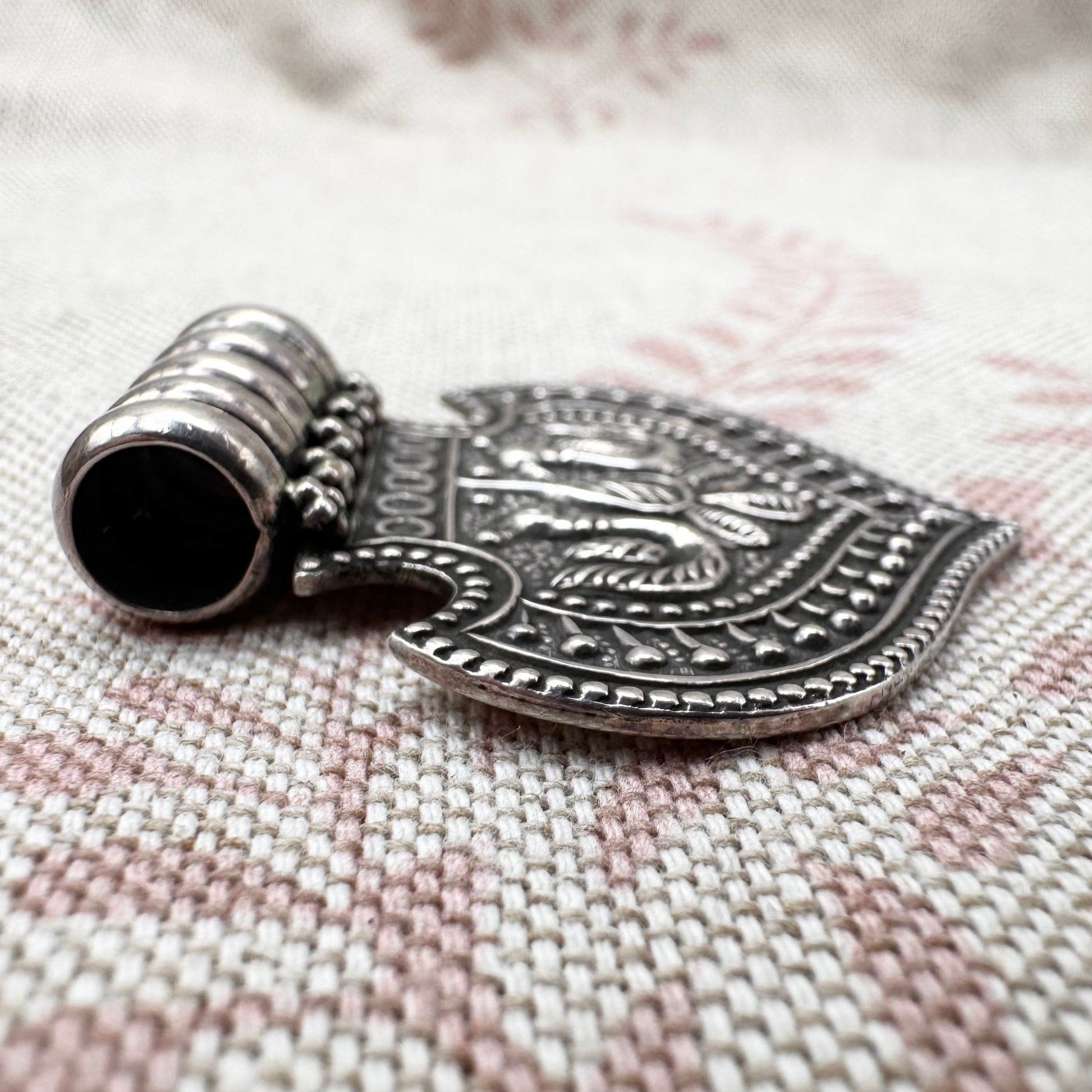 Silver pendant with intricate designs on a textured fabric background