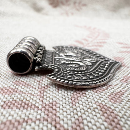 Silver pendant with intricate designs on a textured fabric background