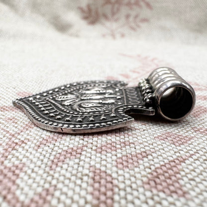 Silver pendant with intricate designs on a textured fabric background
