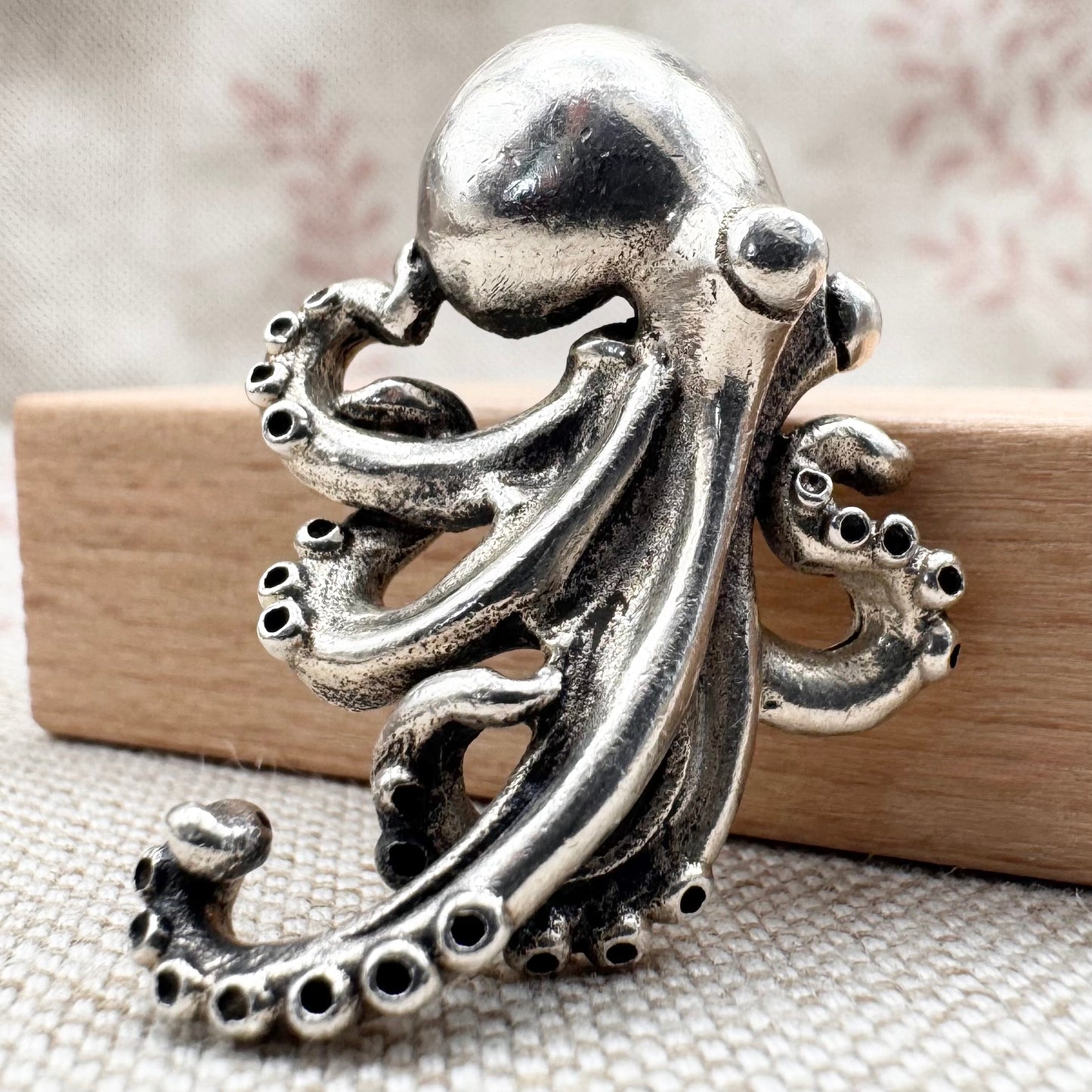 Silver octopus figurine on a textured surface with a wooden block underneath