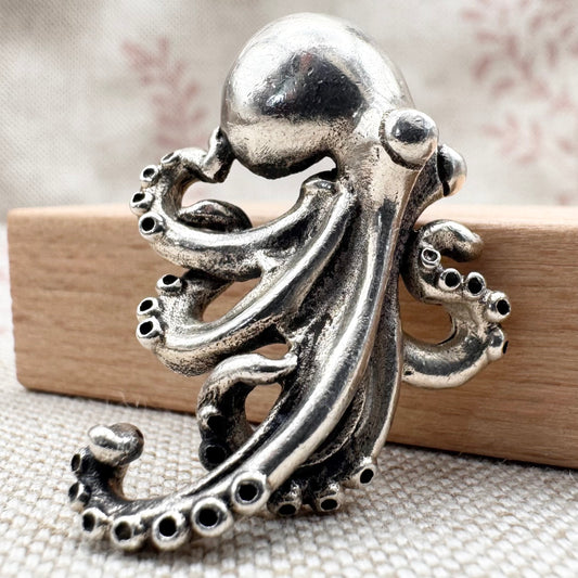 Silver octopus figurine on a textured surface with a wooden block underneath
