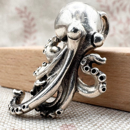 Silver octopus-shaped brooch on a wooden surface with a neutral background