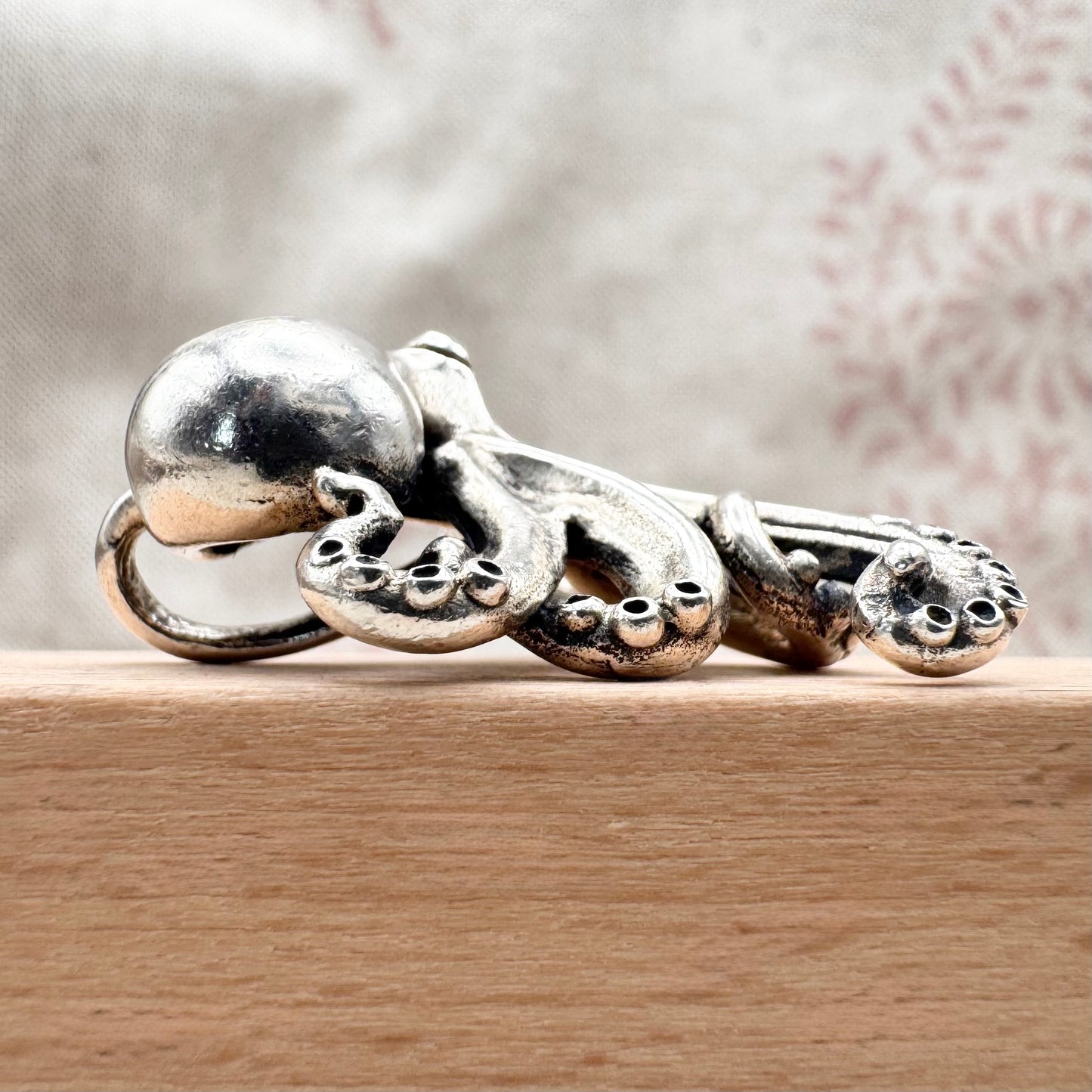 Silver octopus-shaped ring on a wooden surface with a blurred background