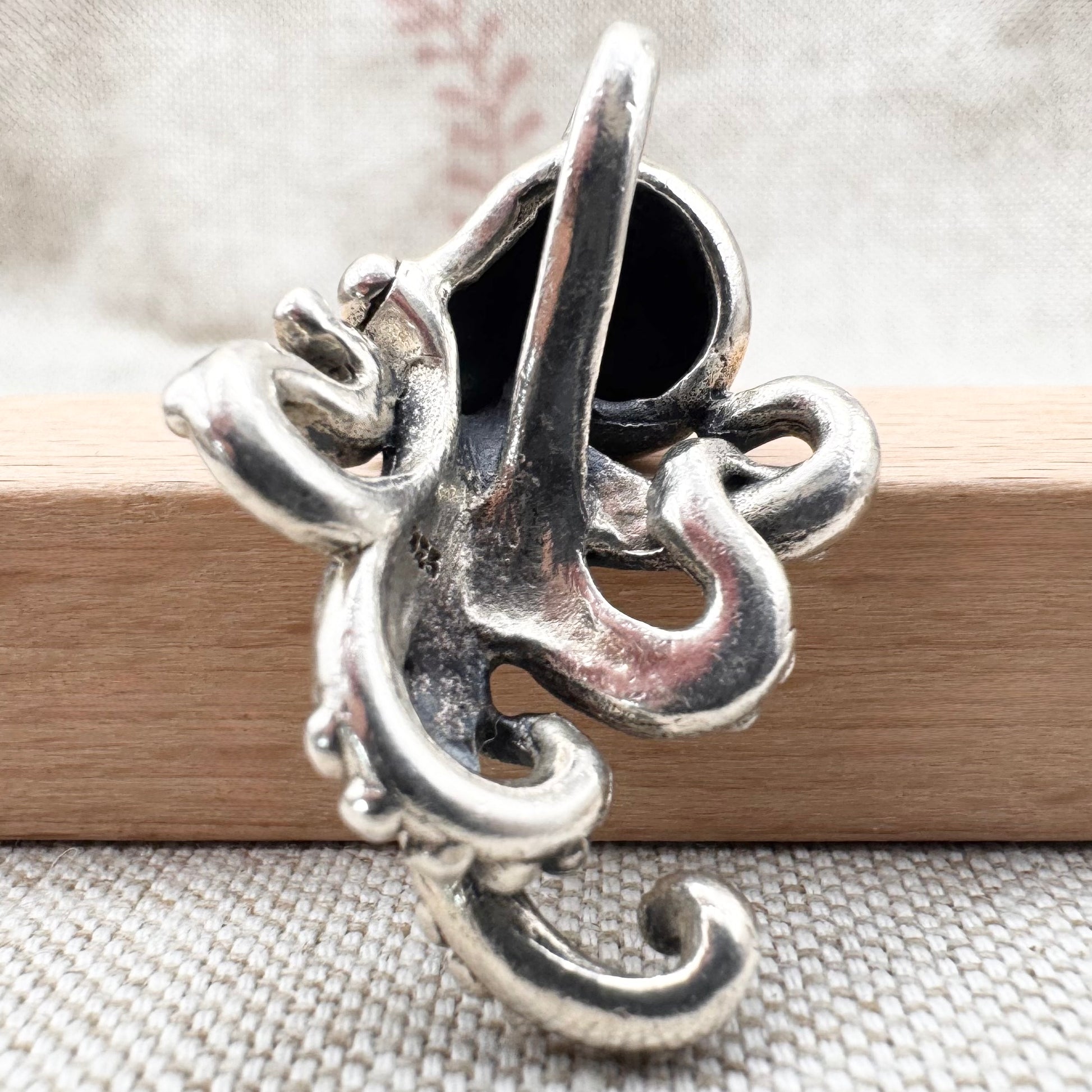 Silver pendant with intricate design on a wooden stick