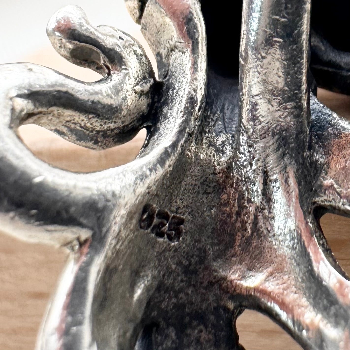 Close-up of a silver pendant with intricate design on a wooden surface